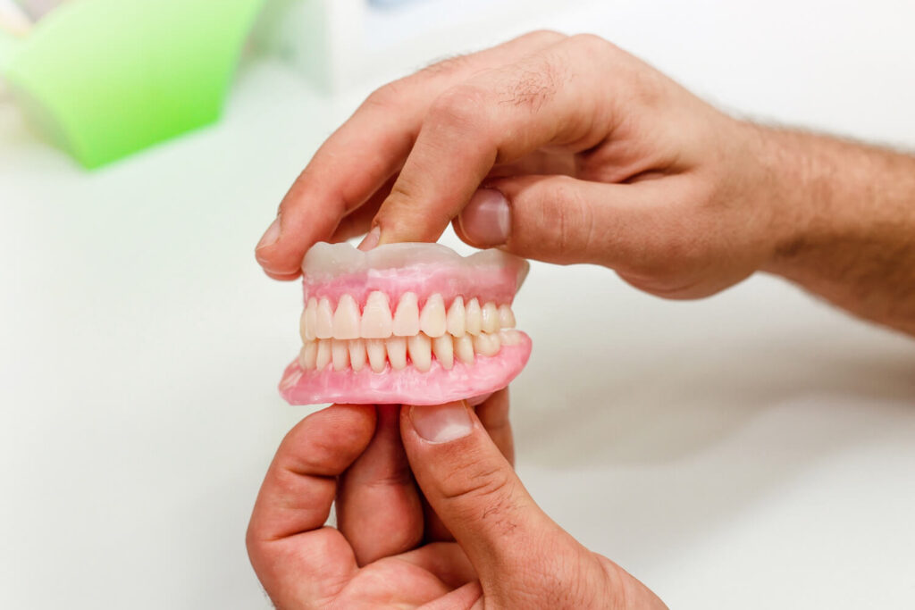 Mãos segurando modelo de prótese total dentária. Opção para trocar dentadura por prótese protocolo em Perdizes na Saraiva Odontologia.