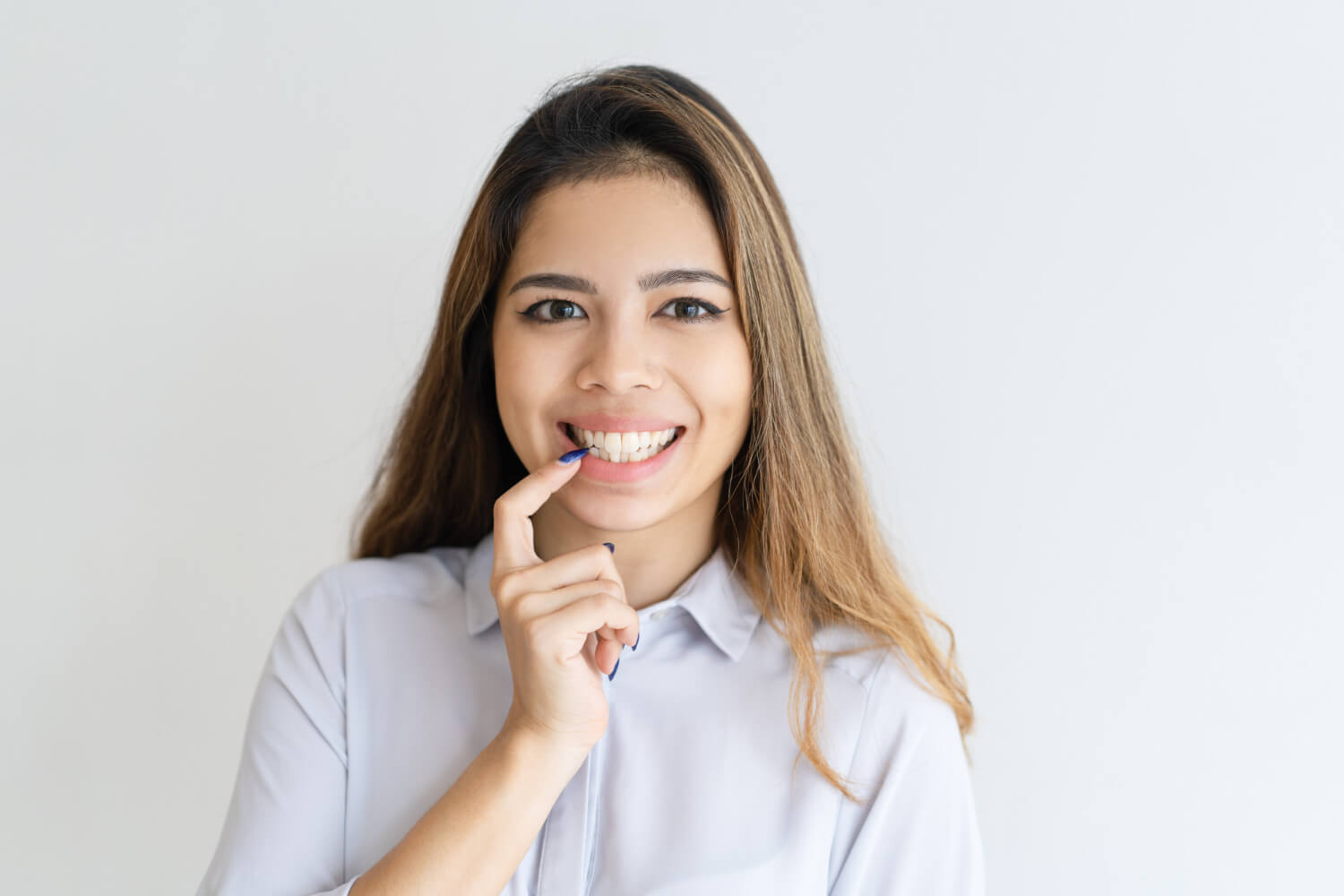 Jovem sorri e aponta para os dentes da frente, demonstrando os resultados das lentes de contato dental sem desgaste em Perdizes.