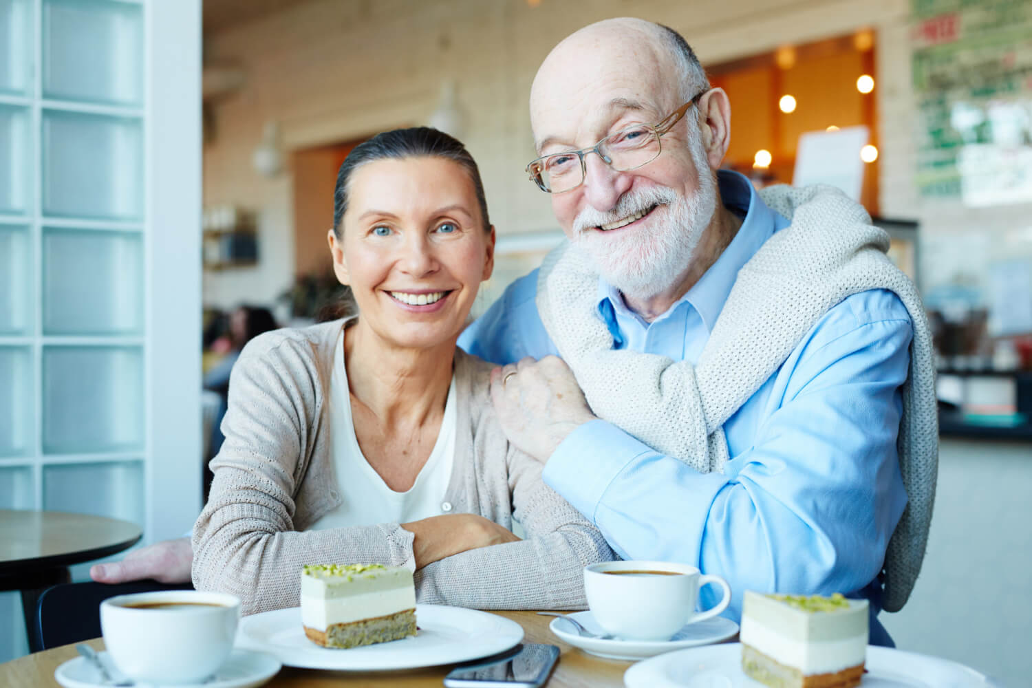Casal idoso sorrindo em um café comendo sobremesa após trocar a dentadura antiga por prótese protocolo na Clínica Saraiva em Perdizes.